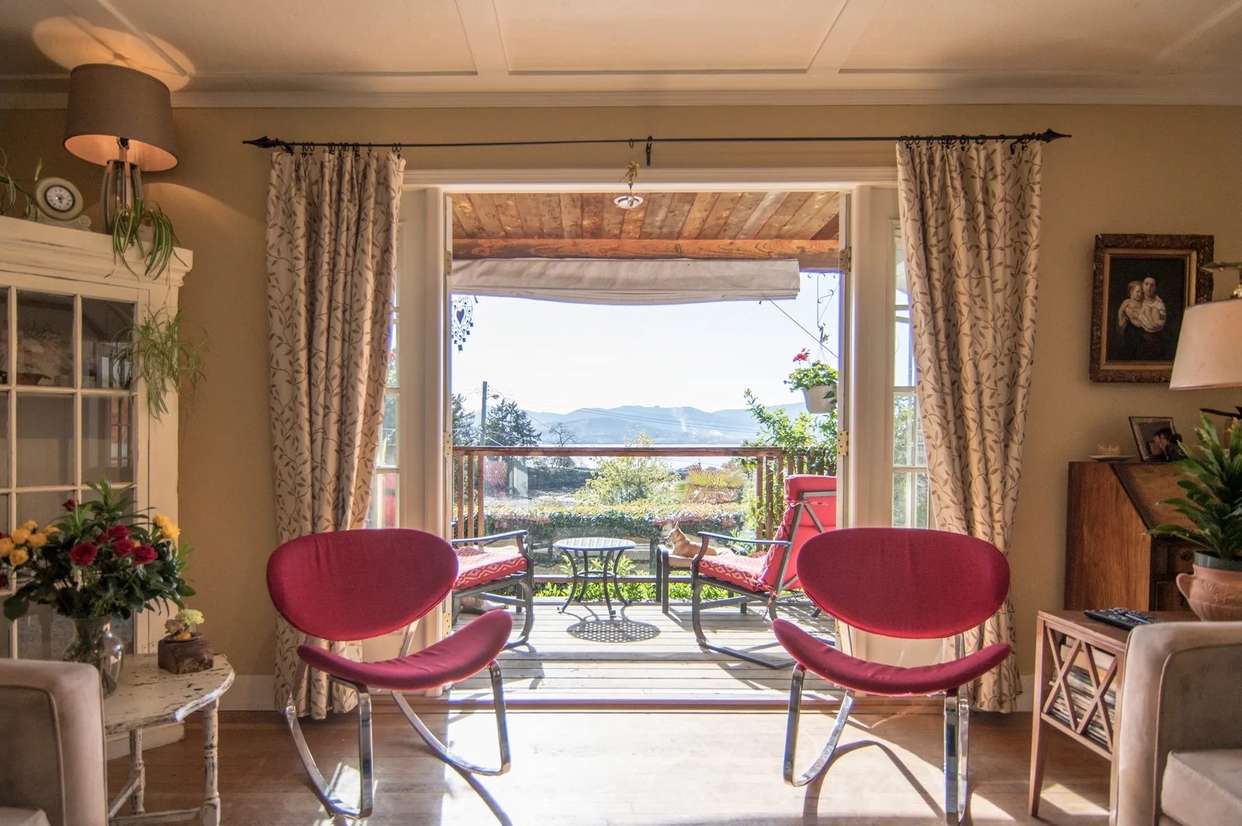 The French-country living room at Bayview Cottage, opening through garden doors to the deck and the water beyond